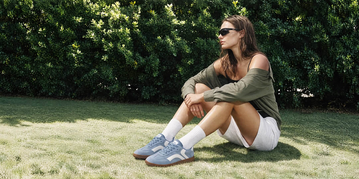 Person seated on grass wearing blue and white Tuopin sneakers and white shorts.